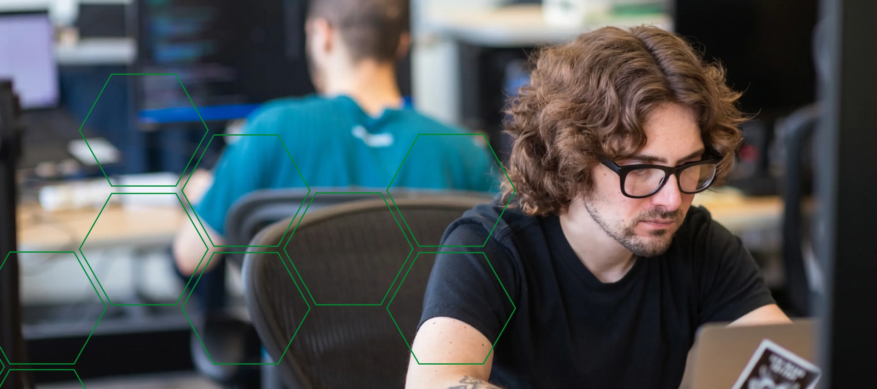 A MojoTech engineer working at a laptop with a colleague in the background.